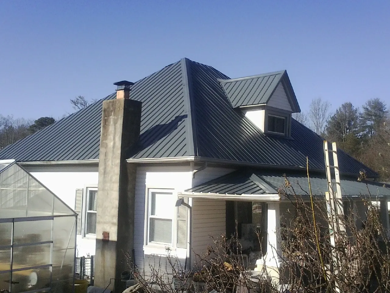 Dark blue standing seam metal roof on a white farmhouse with dormer — Slate & Tile Roof Repair by Roofing Brothers in Yorktown Heights