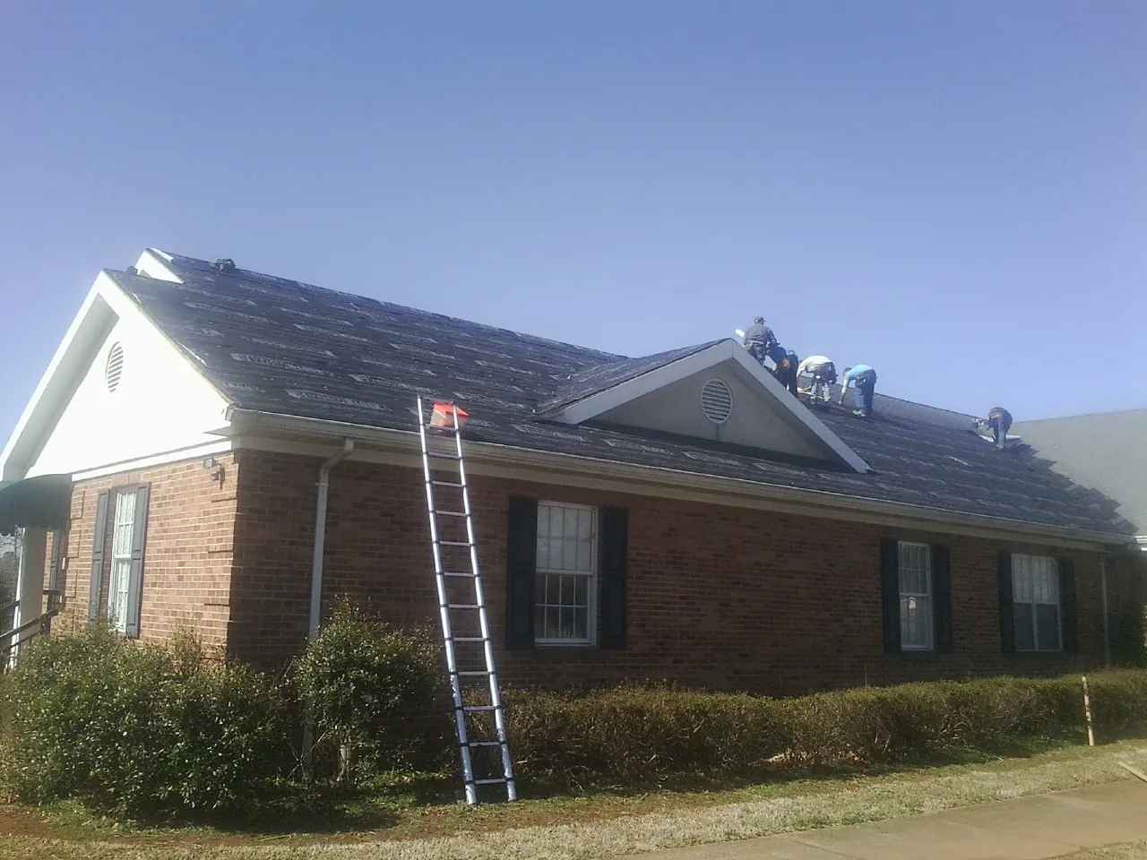 Crew tearing shingles off a brick ranch roof with a ladder set — Metal Roof Repair work by our crew in Yorktown Heights