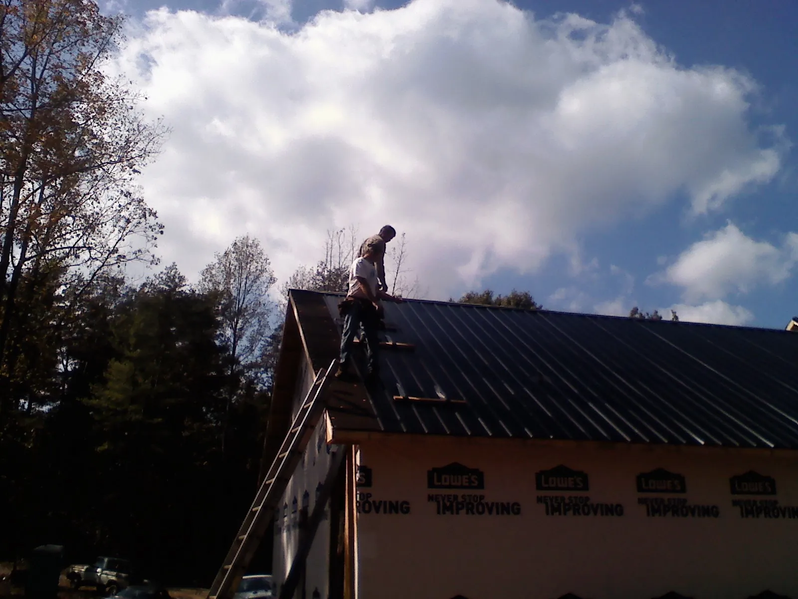 Roofer fastening dark metal panels high against a cloudy sky, from a Roof Inspection job in Yorktown Heights