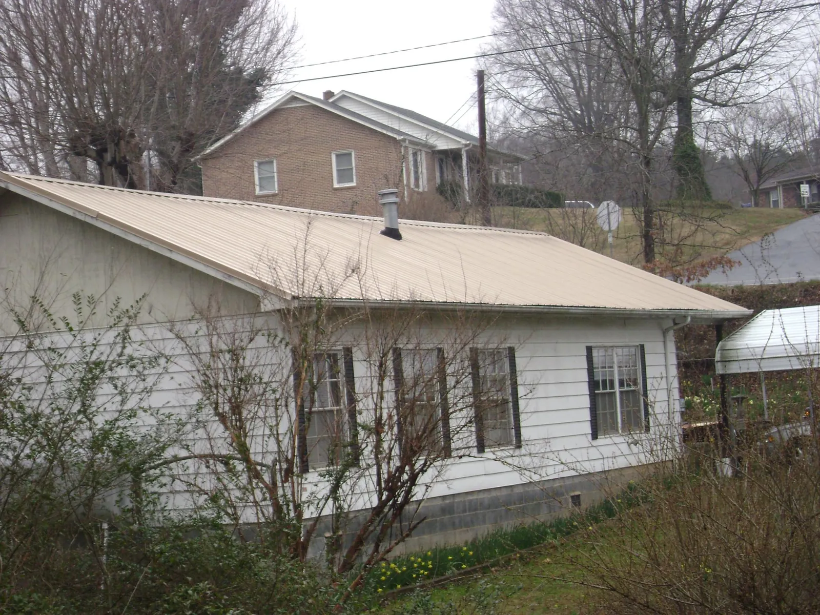 Tan metal roof on a white sided house set into a hillside — Commercial Roofing by Roofing Brothers in Yorktown Heights
