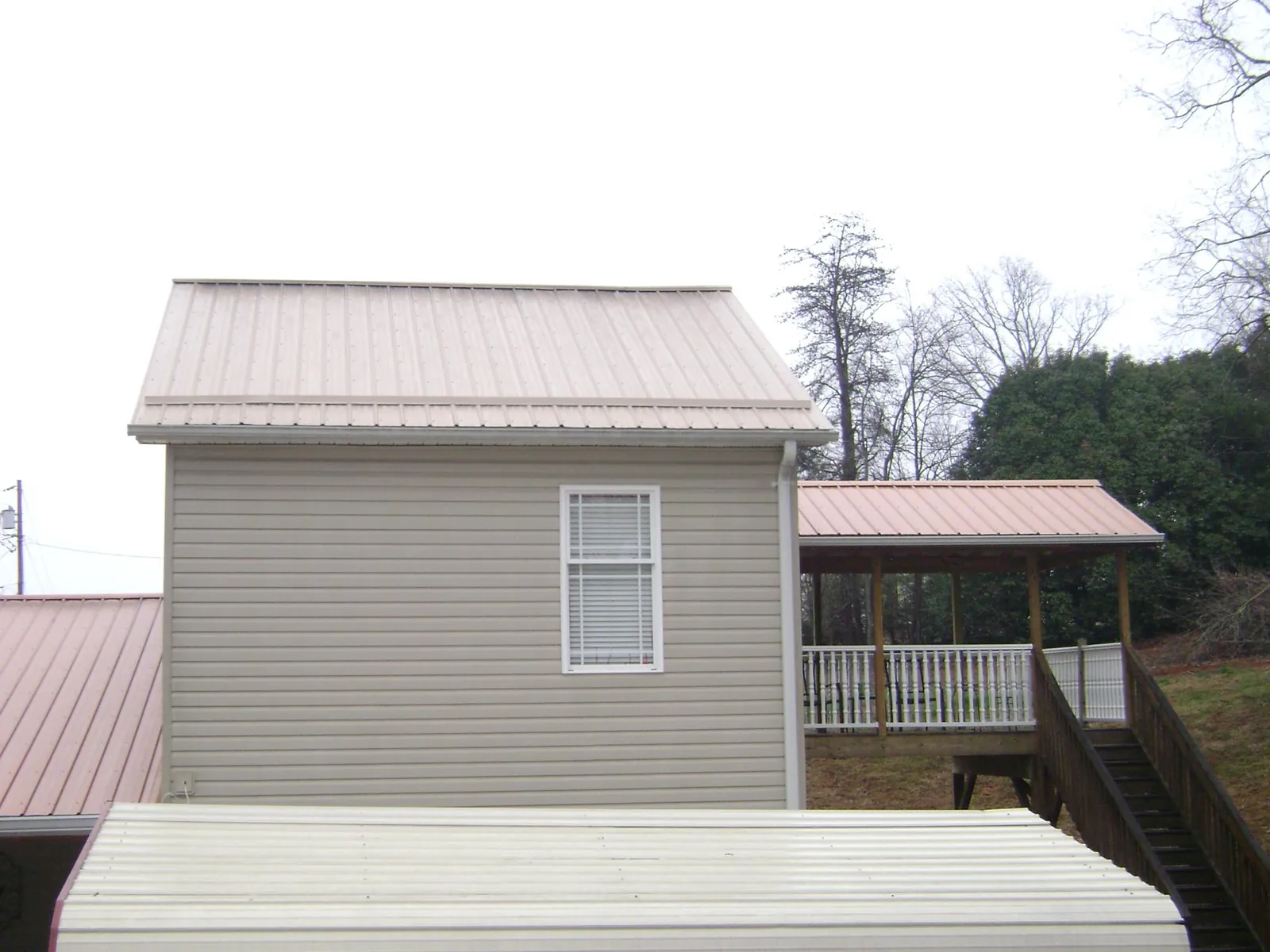 Tan metal roofs on a two story addition and attached porch, from a Roof Replacement job in Yorktown Heights